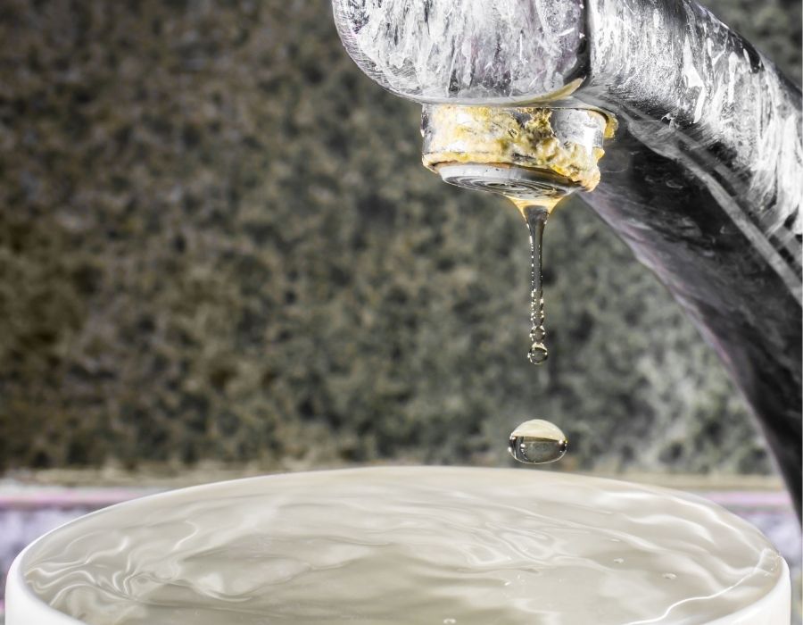 Close-up of kitchen faucet with hard water buildup and dripping leak indicating plumbing repair needs
