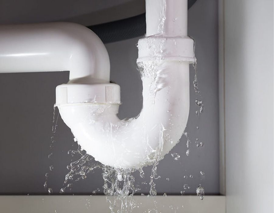 plumbing-emergency Leaking PVC drain pipe under kitchen sink causing water damage and requiring emergency plumbing repair