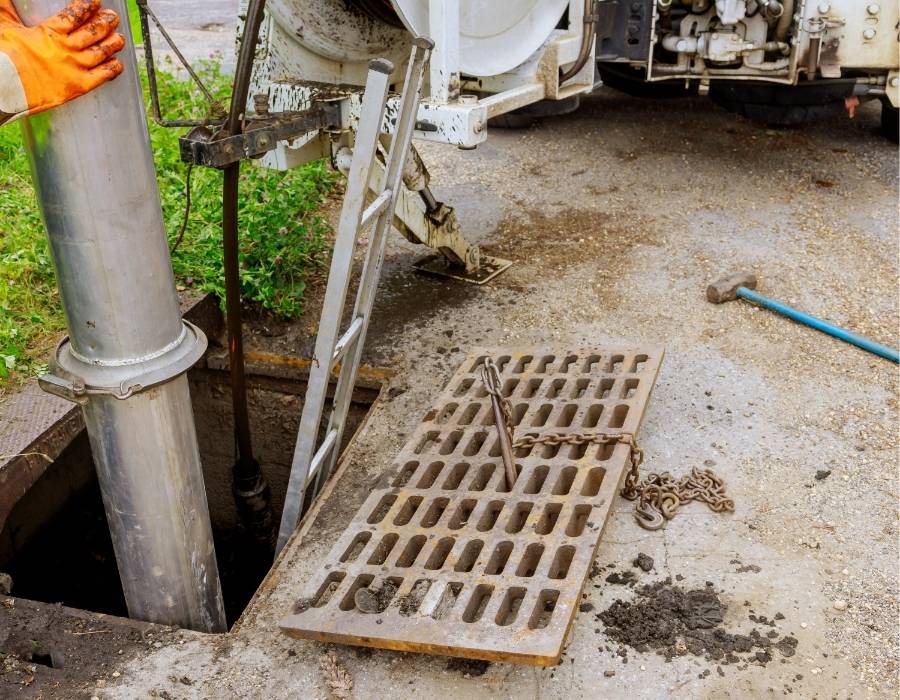 pro-master-services-plumbing-and-drain-services Plumbing technician using vacuum truck to clean storm drain or sewer line through access grate in commercial area