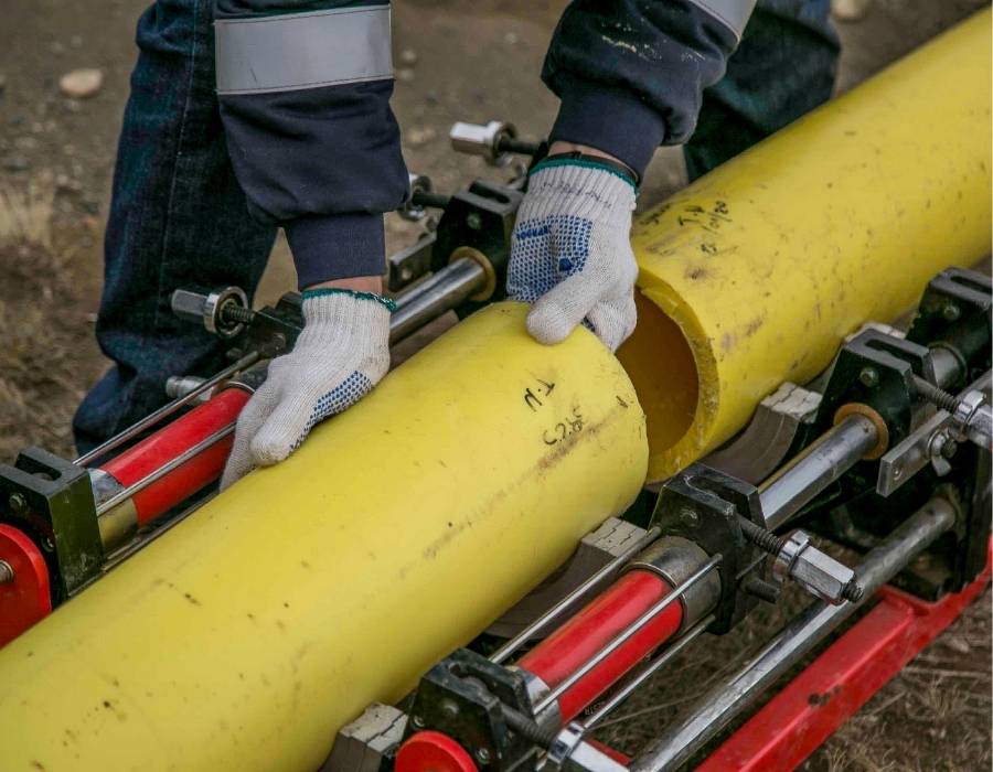Technician aligning large yellow polyethylene gas pipe for fusion welding during underground utility installation