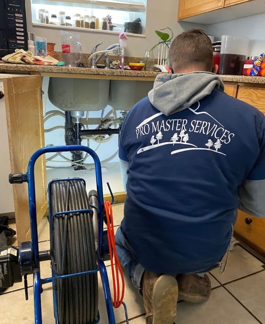 Professional plumber from Pro Master Services using a drain inspection camera to diagnose kitchen sink plumbing issue in a residential home