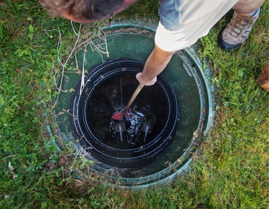 Technician inspecting residential septic tank through open lid on grassy lawn