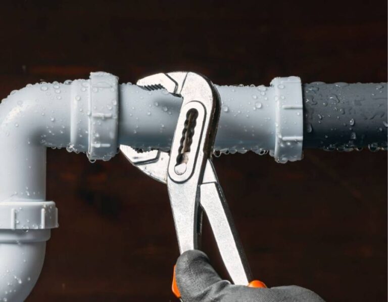Plumber tightening wet PVC drain pipe with adjustable wrench during emergency plumbing repair