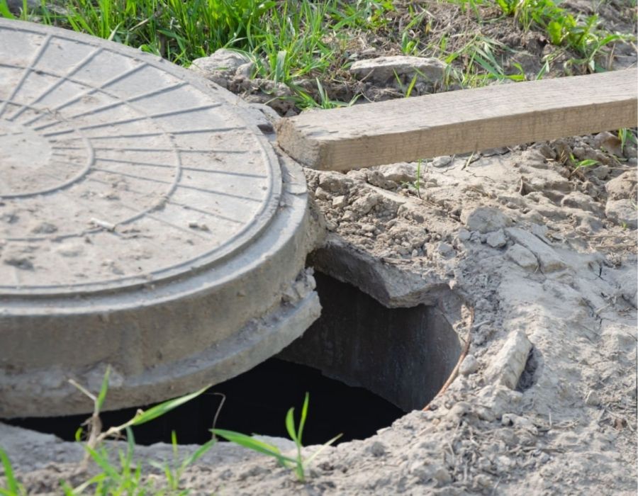 Partially opened sewer access point on residential property with exposed concrete lid