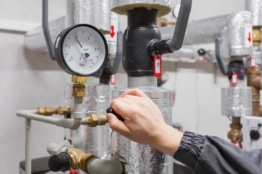 Plumber adjusting pressure valve on a commercial plumbing system with insulated pipes and bar gauge