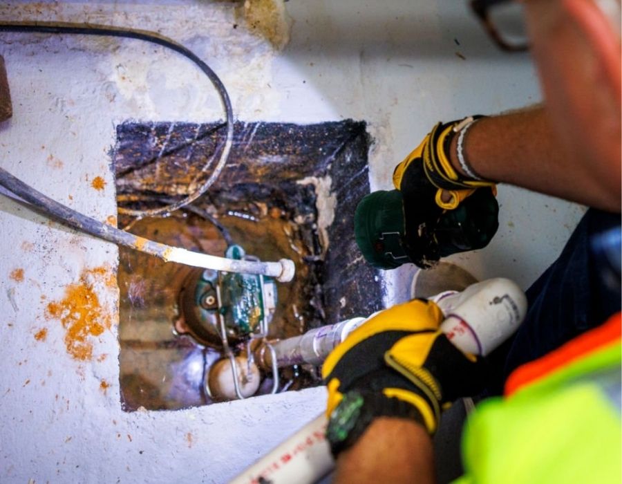 Plumber inspecting sump pump system for leak or failure in residential basement